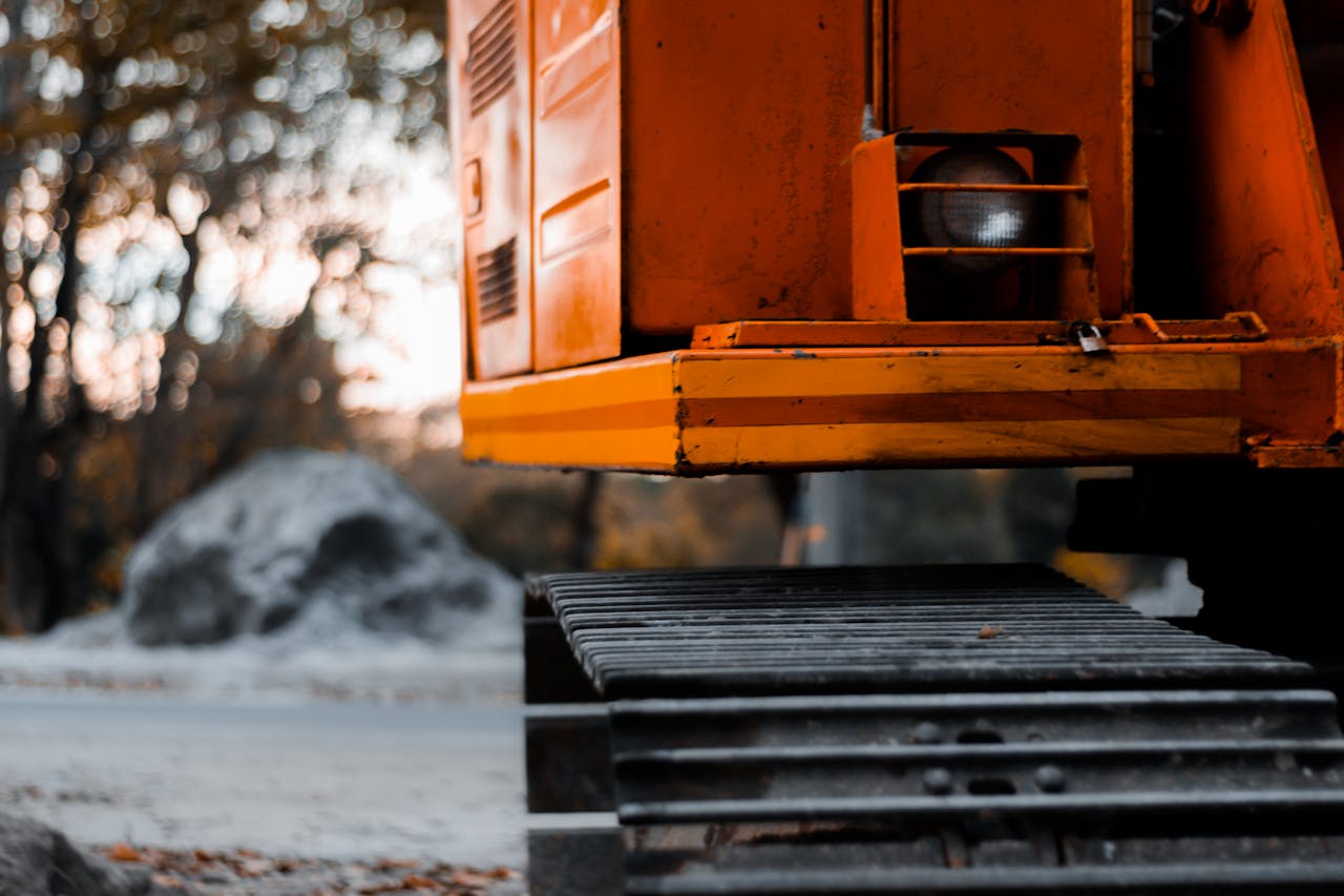 Close-up shot of an orange excavator with tracks in an outdoor setting during the day.