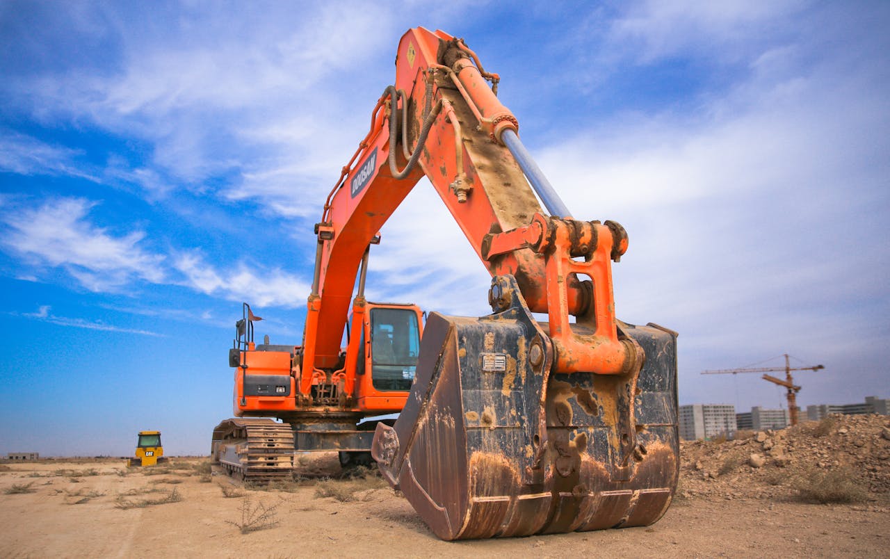 about-03 A large orange excavator working on a construction site under a blue sky.