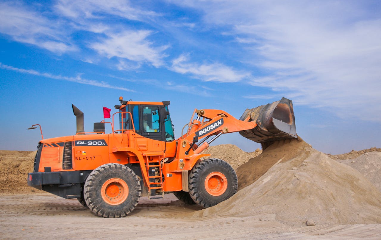 about-01 An orange bulldozer at work, moving sand under a clear blue sky on a construction site.